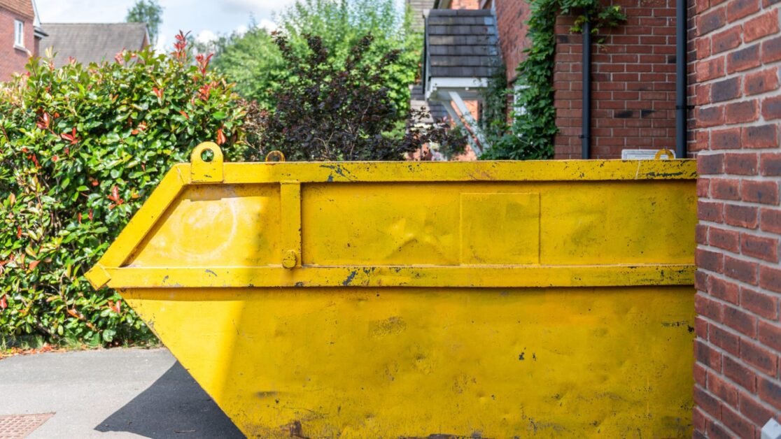 A large size yellow colour skip hire placed infront of a private property