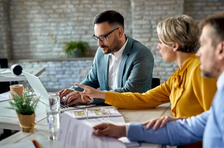 Real estate agent using laptop while having a meeting with a couple in the office.